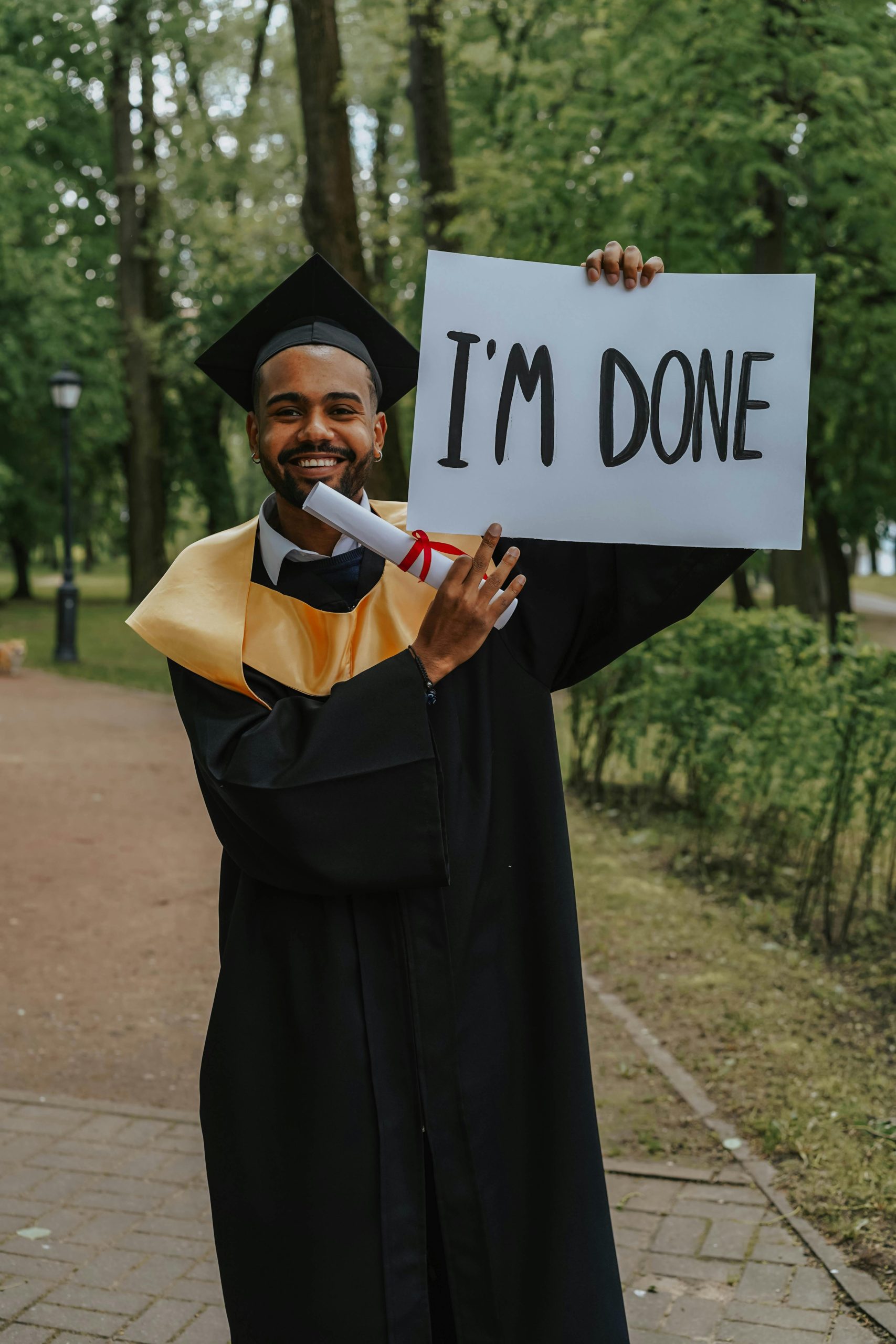 Graduating student holding 'I'm Done' sign in outdoor park setting